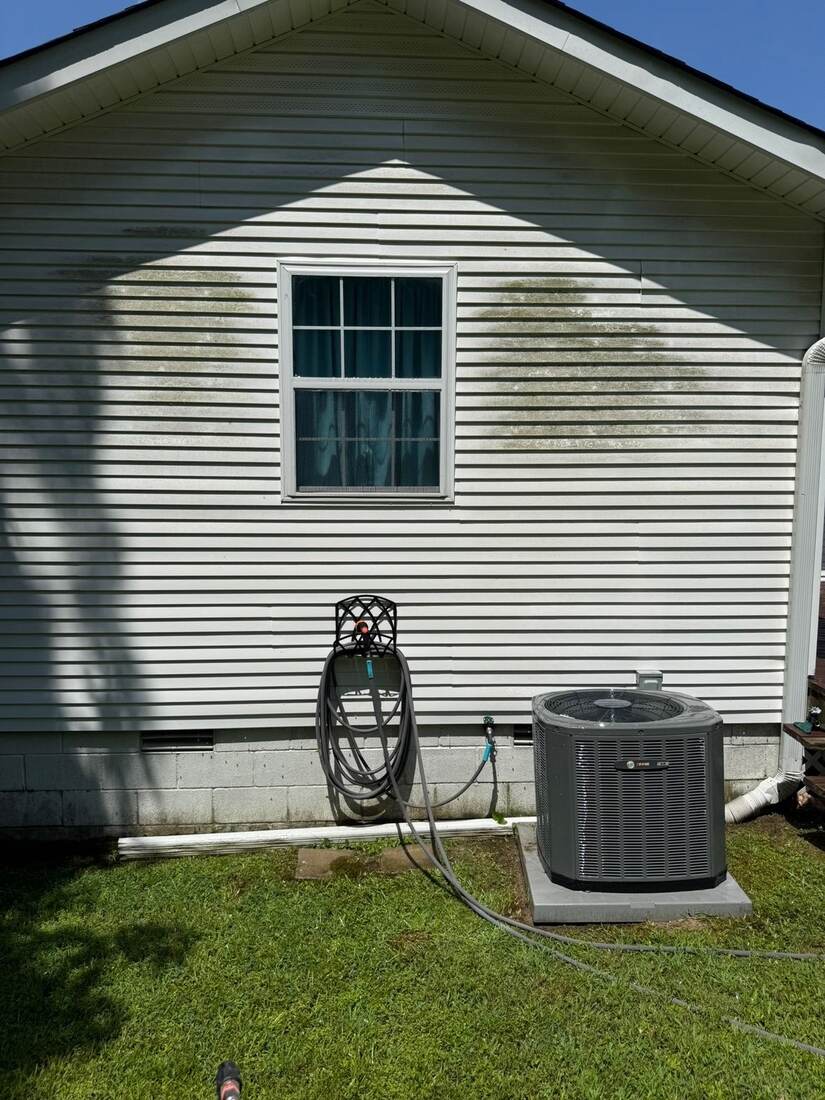 Gable siding with green mildew streaks near a window and AC unit, before cleaning